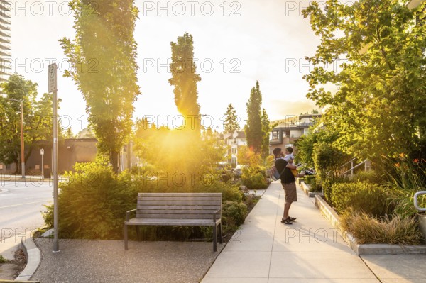 Father enjoying quality time with his baby while strolling through a vibrant vancouver park, basking in the warm glow of the setting sun, captures a heartwarming family moment