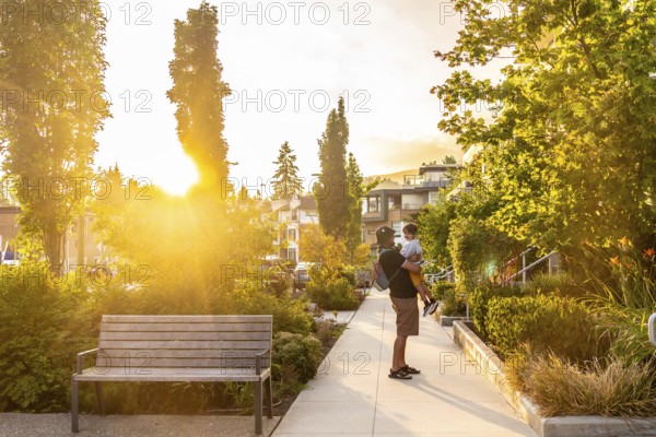 Father holding his son in a residential neighborhood of vancouver, british columbia, during a beautiful sunset, enjoying quality time together in a peaceful urban setting