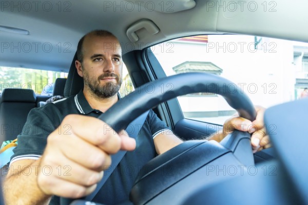 Bearded man driving a modern car in kamloops, british columbia, with a child visible in the back seat, enjoying a summer road trip through the city streets