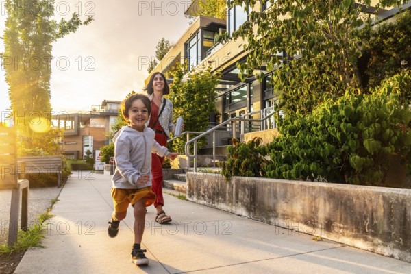 Happy child running joyfully on the sidewalk in vancouver, british columbia, canada, with mother walking closely behind during a beautiful sunset near their home