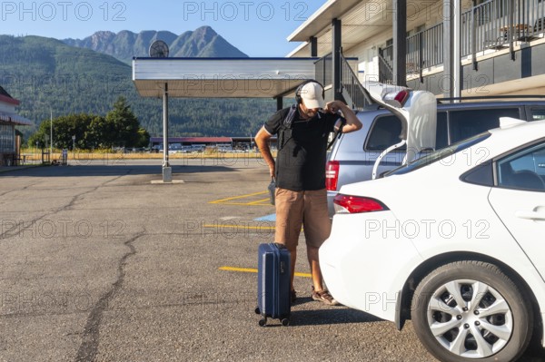 Young backpacker retrieving luggage from the car trunk, preparing for check in at a motel while enjoying a road trip across the country, embracing adventure and freedom