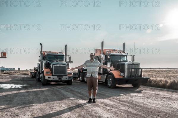 Trucker is proudly showing his two big orange trucks in hemlock grove boardwalk, a scenic rest area in the canadian rockies, enjoying a moment of rest during a long haul journey