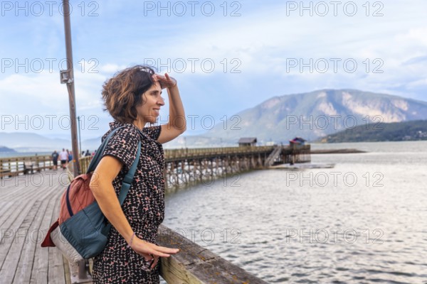 Female tourist shielding her eyes from the sun while enjoying the scenic view of the salmon arm wharf and shuswap lake in british columbia, canada, on a summer day