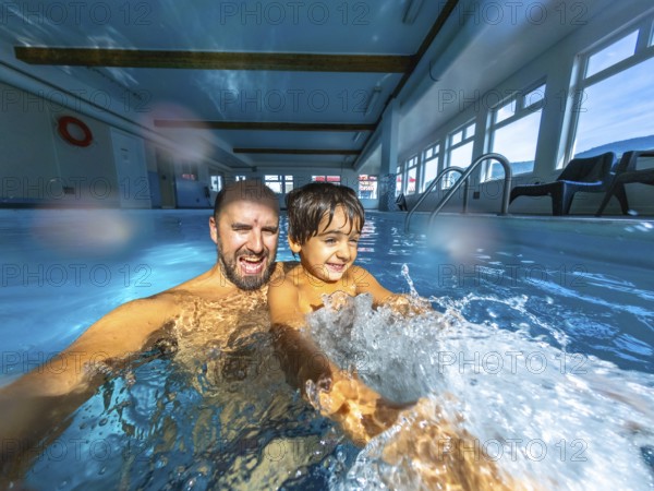 Father and son enjoying playful moments while splashing in an indoor swimming pool, creating a joyful atmosphere filled with laughter and cherished memories together