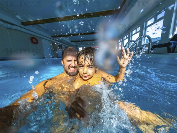 Father and son are having fun in an indoor pool, splashing and playing together, creating a moment of joyful connection and shared activity