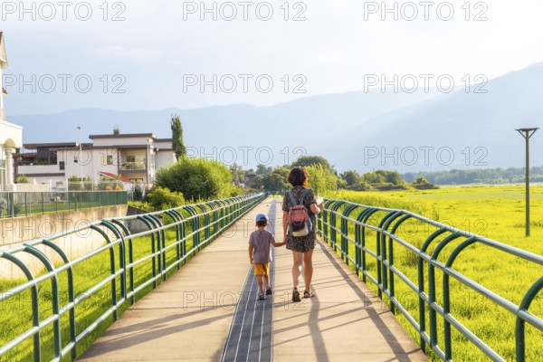Mother and son enjoying a leisurely stroll on a pedestrian bridge, surrounded by lush greenery and mountains in the picturesque city of salmon arm, british columbia, canada