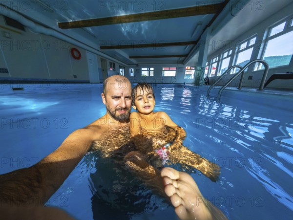 Father and son are taking a selfie while having fun and enjoying time together in a swimming pool during their vacation, creating a cherished memory