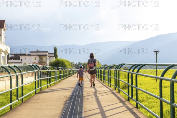Mother and son enjoying a leisurely stroll on a pedestrian bridge in salmon arm, british columbia, surrounded by lush greenery and majestic mountains