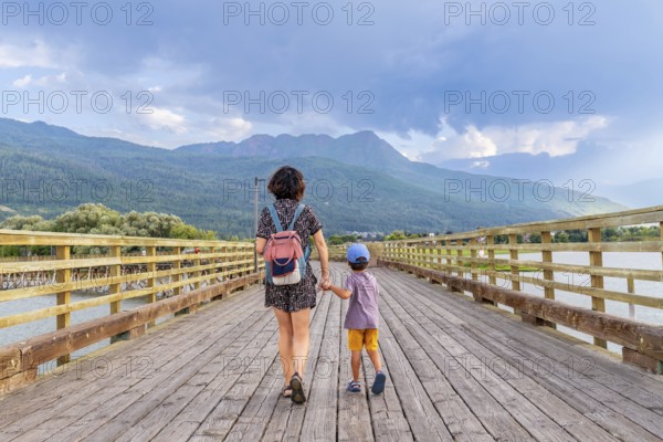 Mother and her son are enjoying a leisurely stroll across a long wooden pier, surrounded by the serene beauty of a lake and majestic mountains in salmon arm, british columbia