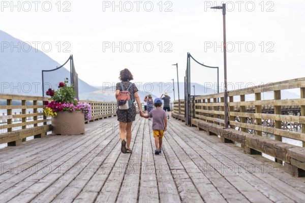 Mother and son enjoying a leisurely stroll along a picturesque wooden pier in salmon arm, british columbia, surrounded by stunning natural beauty and a tranquil atmosphere