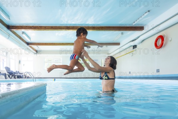 Smiling mother catching her joyful son mid air as he jumps into the pool, enjoying a playful moment of bonding and fun during their swimming session