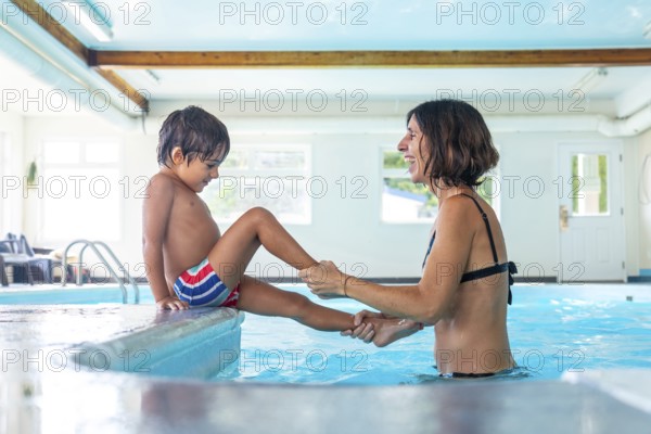 Mother playfully holding her son's legs as he prepares to enter the pool, capturing a heartwarming moment of family bonding and joy during a fun summer day together