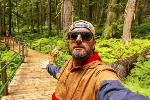 Hipster tourist taking a selfie while walking and showing the hemlock grove boardwalk in an ancient rainforest near revelstoke, british columbia, canada, during a sunny summer day