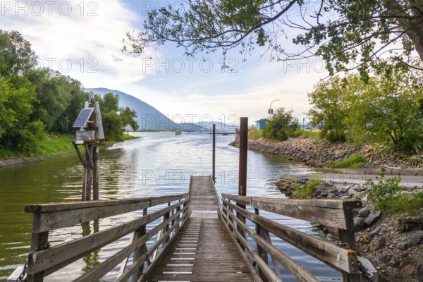 Wooden pier with solar powered navigation light extending into shuswap lake in salmon arm, british columbia, features calm water, mountains, and lush greenery under a cloudy sky