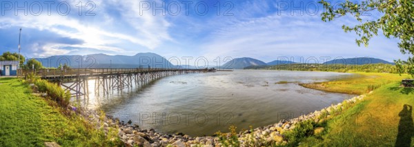 Panoramic view of a long wooden pier stretching into the tranquil waters of shuswap lake, surrounded by the scenic beauty of salmon arm, british columbia, on a sunny day