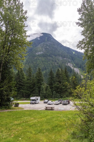 Clouds partially covering mountain peak near parking lot with parked recreational vehicles and cars near hemlock grove boardwalk in the canadian rockies, british columbia, canada