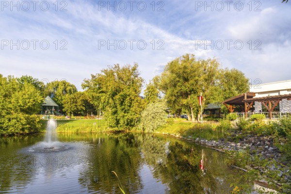 Tranquil pond with a fountain in a public park in salmon arm, british columbia, canada, surrounded by lush trees and a gazebo, reflecting the serene beauty of nature