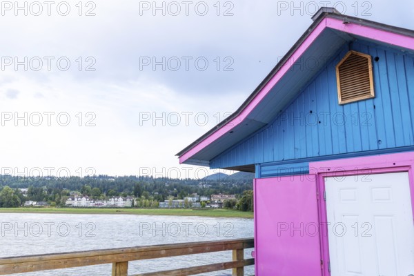 Pink and blue painted building standing on a wooden pier overlooking shuswap lake and the cityscape of salmon arm, british columbia, on a cloudy day