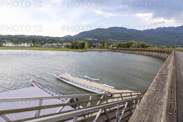 Dragon boats are tied up at a floating dock near a wooden pier, with the city of salmon arm and the shuswap mountains in the background on a cloudy summer day in british columbia, canada