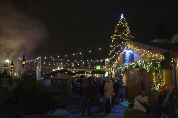 A lively Christmas market at night with illuminated wooden stalls and lots of visitors, Winterberg, North Rhine-Westphalia, Germany