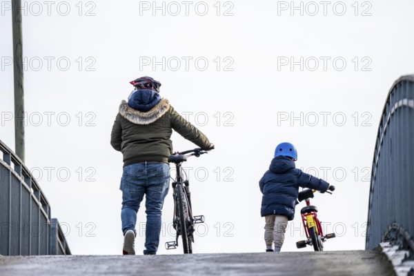 Father and son push their bikes up a steep bicycle bridge together