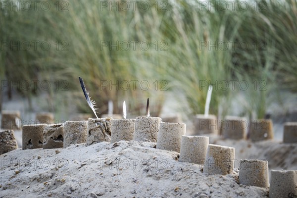 Sandcastle on the beach, detailed view of a sand castle with small towers and dug in the sand, behind it dunes with beach grass in a soft background, diffuse daylight and quiet, playful coastal atmosphere, Schillig, Lower Saxony, Germany