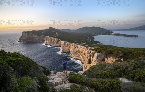 Tourist in front of coastal landscape at sunset, steep cliffs by the sea, cliffs in the evening light, Capo Caccia, Alghero, Sardinia