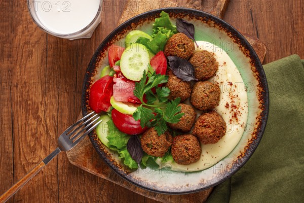 A plate holds falafel balls, tahini, salad with tomatoes and cucumbers, and a drink. The setting is warm and inviting, perfect for a midday meal with fresh ingredients