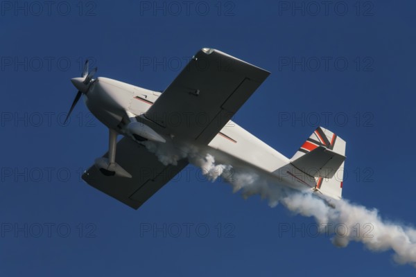 Stunt aerobatic plane performing stunts in blue sky with smoke trail. Concept of speed, difficulty, precision, risk, challenge
