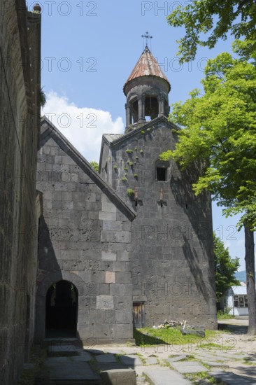 Stone church tower with bell tower, surrounded by trees and shade, blue sky visible, Sanahin monastery, town of Sanahin, UNESCO World Heritage Site, Lorikeet province, Armenia