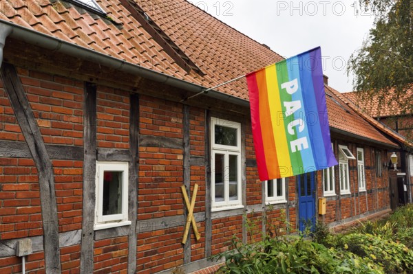 International peace flag on a private house, pace flag, rainbow flag with the inscription peace, symbol of diversity and peaceful coexistence, yellow X symbol against nuclear waste transportation, Lüchow-Dannenberg, Wendland, Germany