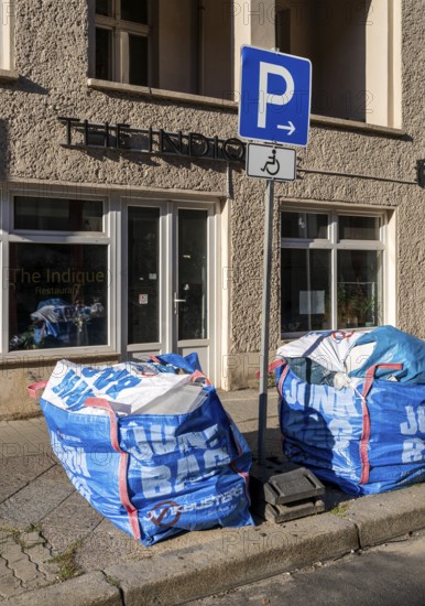 Plastic bags with construction waste lie on the side of the road and block access to a parking space for the disabled, Berlin, Germany