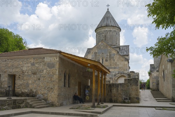Church building with tower and stone walls, surrounded by trees, in cloudy sky, Haghartsin monastery, Hagarzin, Tavush province, Armenia