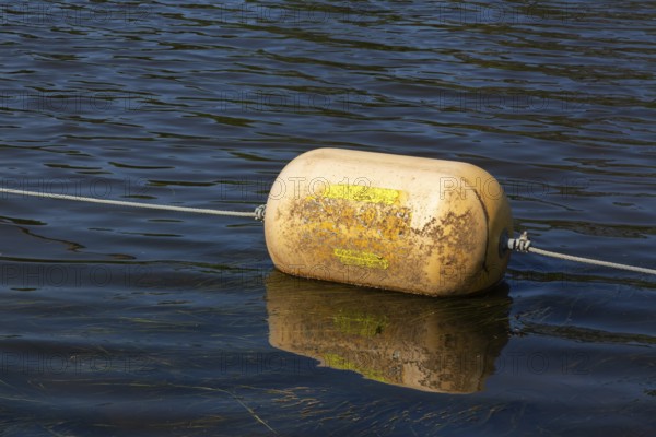 Yellow cautionary navigation buoy on river water surface serving to warn, signal or indicate of a hazard beyond, Terrebonne, Quebec, Canada