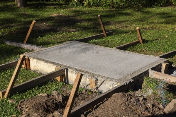 Wooden concrete pouring forms and freshly poured raised concrete base for anchoring a bench in public park, Quebec, Canada