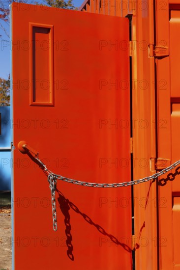 Entrance door kept opened with a chain on bright fluorescent orange painted metal box shaped shipping container, Quebec, Canada