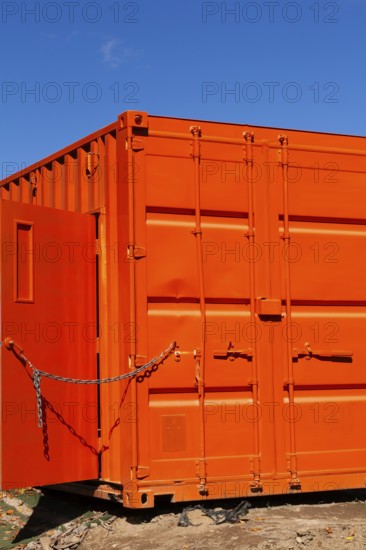 Locked bright fluorescent orange painted metal box shaped shipping container with door kept opened with a chain, Quebec, Canada