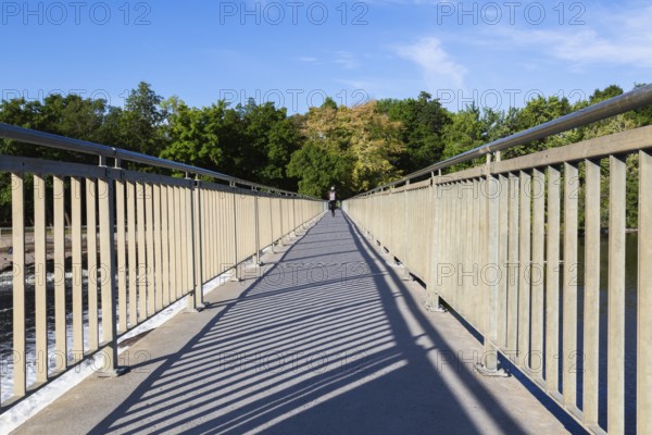 Electric scooter rider on pedestrian walkway on top of water flow control Moulin Neuf dam over Des Mille-Iles river in summer, Old Terrebonne, Quebec, Canada