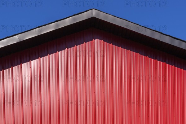 Close-up of building with black metal trim gable roof edge and cladded with red sheet metal siding, Quebec, Canada