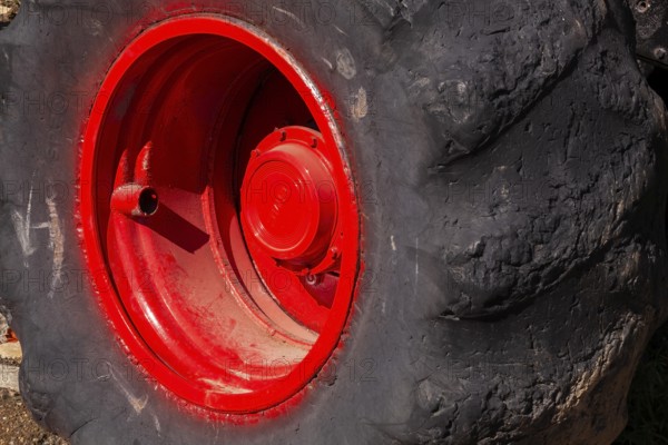 Close-up and rear side view of large heavy duty black rubber tire mounted on red rim on monster truck vehicle, Quebec, Canada