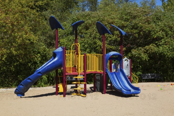 Kids playground equipment with slides, climbers and monkey bars installed in sandy ground in city park in late summer, Parc du Grand-Coteau, Mascouche, Quebec, Canada