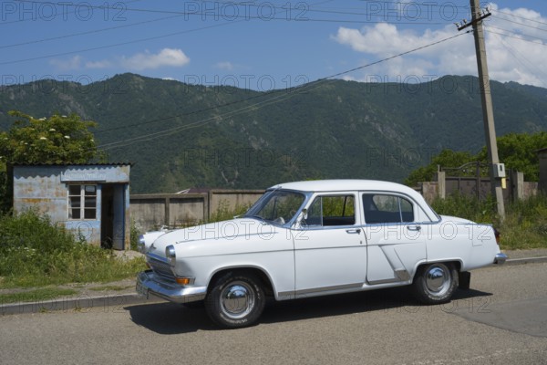White vintage car on a country road with mountain backdrop and blue sky in summer, GAZ M-21 Volga, Odsun, Odzun, Debed Gorge, Lorikeet Province, Armenia