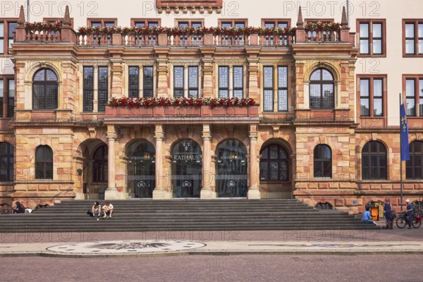 Town Hall, architect Georg von Hauberrisser, neo-Renaissance style, entrance, doors, round arches, columns, sandstone building material, façade with windows and flower boxes, pedestrians and seated people as a secondary motif, diffuse light, slightly sunny, Schlossplatz square, Wiesbaden, state capital, district-free city, Hesse, Germany