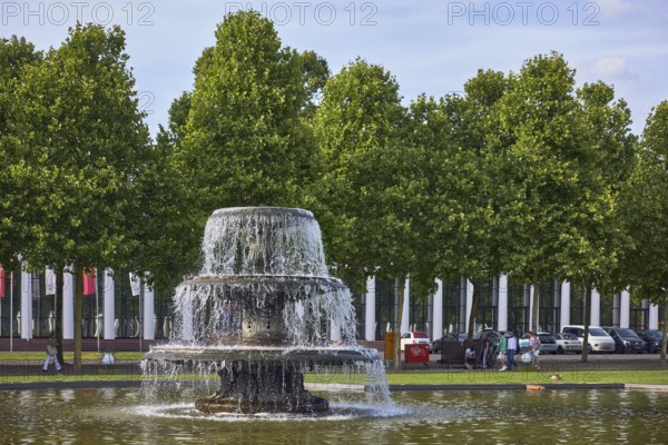 Cascade fountain, lawn, trees, general buildings, pedestrians as accessories, frozen movement, depth of focus with blurred background, milky blue sky, diffuse light, slightly sunny, bowling green, Kurhausplatz, Wiesbaden, state capital, district-free city, Hesse, Germany