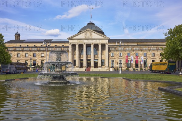Spa hotel, neoclassicism style, architect Friedrich von Thiersch, inscription Aquis Mattiacis, pillars, sandstone building material, garden, green area, lawn, cascade fountain, abstract reflections on the water surface, blue sky, cumulus clouds, evening light, Kurhausplatz, Wiesbaden, state capital, district-free city, Hesse, Germany