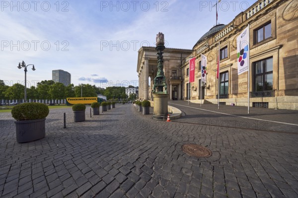 Spa hotel, architectural style neoclassicism, architect Friedrich von Thiersch, building material sandstone, facade with windows, access road, planter, common boxwood (Buxus sempervirens), lantern, access road, advertising banner on flagpole, Rheingau Music Festival, skyscraper, trees, blue sky, cumulus clouds, diffuse light, slightly sunny, evening light, Kurhausplatz, Wiesbaden, state capital, independent city, Hesse, Germany