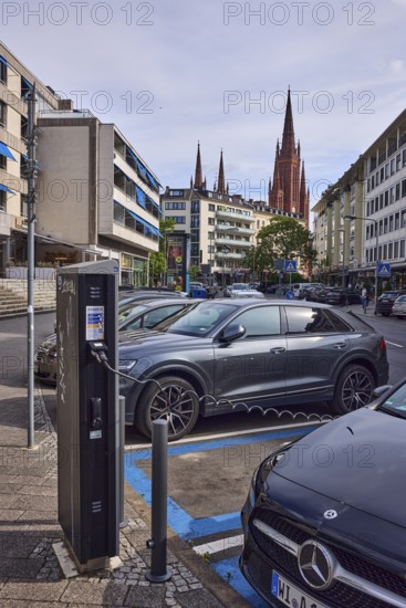 Electric car, charging station for e-cars, charging process, general architecture, residential buildings and commercial buildings, church tower of the market church, cloudy, diffuse light, slightly sunny, street An den Quellen, Wiesbaden, state capital, district-free city, Hesse, Germany
