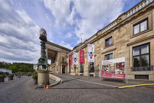 Spa hotel, access road, brick street, entrance area, flags on flagpoles, neoclassical style with elements of Art Nouveau, architect Friedrich von Thiersch, blue sky, cumulus clouds, Nimbostratus clouds, Kurhausplatz, Wiesbaden, state capital, district-free city, Hesse, Germany