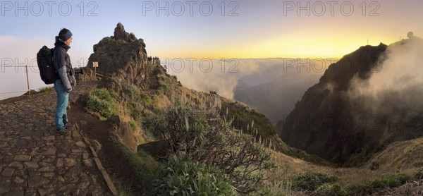 Hiker, woman watching sunrise at Pico do Arieiro, clouds of fog sweeping over mountain peaks, sea of fog, hiking trail PR1, Madeira, Portugal