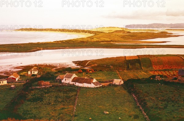 View over thatched farmhouse buildings to Magheraroarty Beach, Meenlaragh, County Donegal, Ireland 1960s